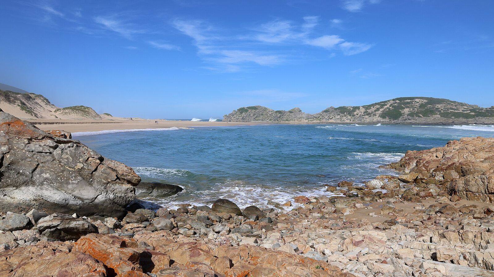 Breed zandstrand bij Plettenberg Bay met golven en bergen op de achtergrond